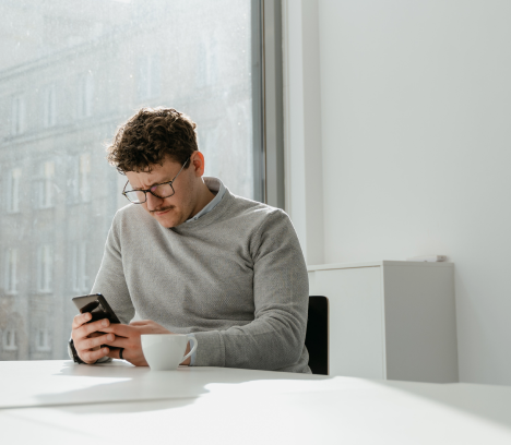 un homme sur son téléphone et qui boit un café
